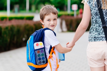 Little 7 years old boy with his mother at road to school. Dressed in white t shirt and shorts