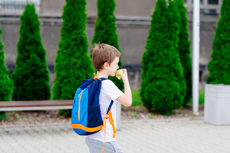 Little 7 years old boy with apple at road to school. Dressed in white t shirt and shortsの写真素材