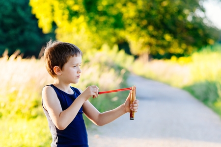 Little boy playing with slingshot at summer afternoon outdoorsの写真素材