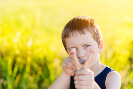Little boy playing with slingshot at summer afternoon outdoorsの写真素材