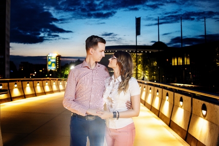 Young couple hugging on the bridge at night. Looking in each other eyes. Engagement session. Girl wears glassesの写真素材