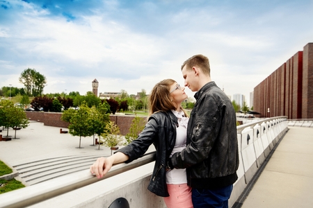 Young couple kissing on the bridge. Engagement session. Dressed in black leather jackets. Girl wears glassesの写真素材