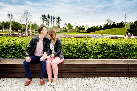 Young couple in love hugging on the bench. Engagement session. Dressed in black leather jackets. Girl wears glassesの写真素材