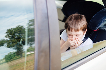 Seven years old small child in the backseat of a car sitting in children safety car seat covers his mouth with his hand - suffers from motion sicknessの写真素材