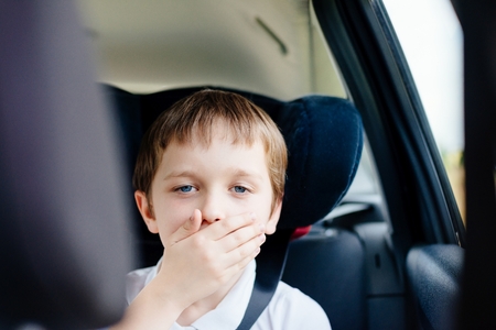 Seven years old small child in the backseat of a car sitting in children safety car seat covers his mouth with his hand - suffers from motion sicknessの写真素材