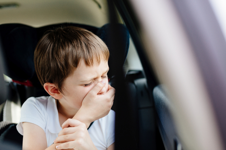 Seven years old small child in the backseat of a car sitting in children safety car seat covers his mouth with his hand - suffers from motion sicknessの写真素材