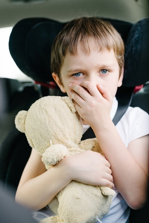 Seven years old small child in the backseat of a car sitting in children safety car seat covers his mouth with his hand - suffers from motion sicknessの写真素材