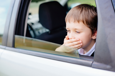 Seven years old small child in the backseat of a car sitting in children safety car seat covers his mouth with his hand - suffers from motion sicknessの写真素材