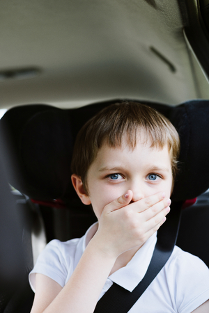 Seven years old small child in the backseat of a car sitting in children safety car seat covers his mouth with his hand - suffers from motion sicknessの写真素材