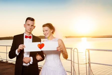 Bride and groom on the pier at sunset. Holding empty card with copyspace. Wedding day. Wedding sessionの写真素材