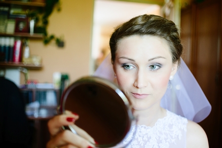 Young bride looking into mirror. Wedding preparations. Bridal morning of a cute lady. Wedding day.の写真素材
