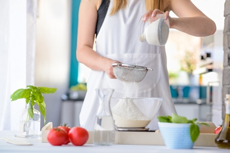 Woman sifting flour through sieve. Woman doing homemade pizza. Dressed in white pinnyの写真素材