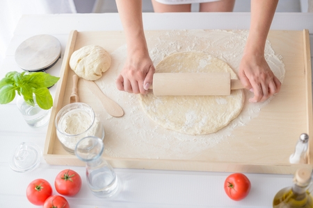Woman rolling pizza dough using rolling pin. Woman doing homemade pizza. Dressed in white pinnyの写真素材