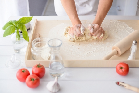 Woman kneading pizza dough on wooden pastry board. Woman doing homemade pizza. Dressed in white pinnyの写真素材