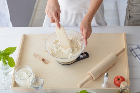 Woman mixing pizza dough with wooden spatula. Woman doing homemade pizza. Dressed in white pinnyの写真素材