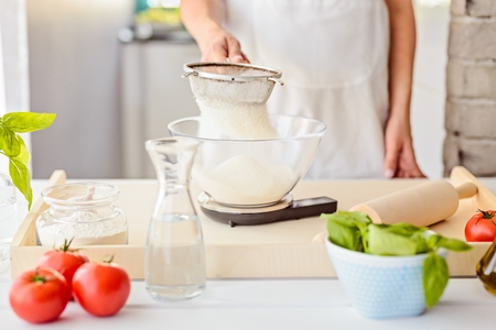 Woman sifting flour through sieve. Woman doing homemade pizza. Dressed in white pinnyの写真素材