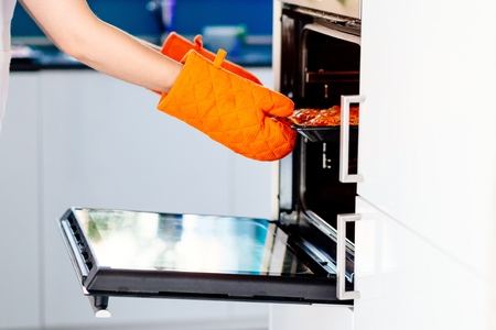 Woman pulling a pizza from electric oven. Woman doing homemade pizza. Dressed in white pinnyの写真素材