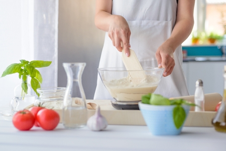 Woman mixing pizza dough with wooden spatula. Woman doing homemade pizza. Dressed in white pinnyの写真素材