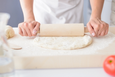 Woman rolling pizza dough using rolling pin. Woman doing homemade pizza. Dressed in white pinnyの写真素材