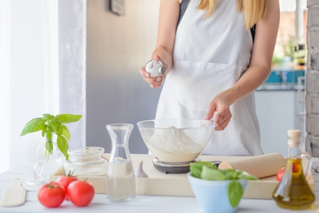 Woman adding salt to flour. Woman doing homemade pizza. Dressed in white pinnyの写真素材