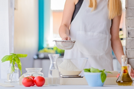 Woman sifting flour through sieve. Woman doing homemade pizza. Dressed in white pinnyの写真素材