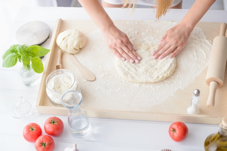 Woman kneading pizza dough on wooden pastry board. Woman doing homemade pizza. Dressed in white pinnyの写真素材