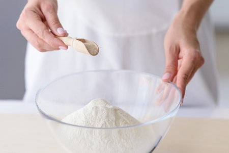 Woman adding powdered yeast to flour. Woman doing homemade pizza. Dressed in white pinnyの写真素材