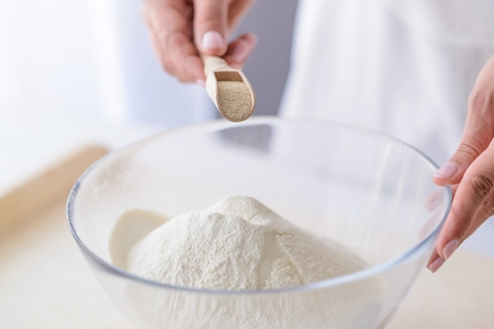 Woman adding powdered yeast to flour. Woman doing homemade pizza. Dressed in white pinnyの写真素材