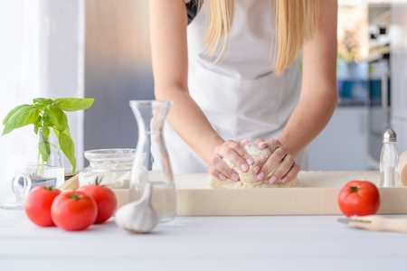 Woman kneading pizza dough on wooden pastry board. Woman doing homemade pizza. Dressed in white pinnyの写真素材