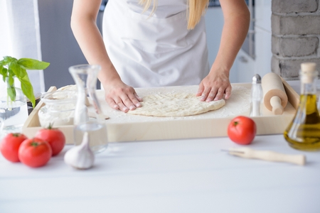 Woman kneading pizza dough on wooden pastry board. Woman doing homemade pizza. Dressed in white pinnyの写真素材