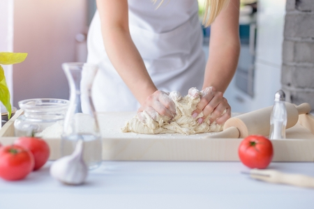 Woman kneading pizza dough on wooden pastry board. Woman doing homemade pizza. Dressed in white pinnyの写真素材
