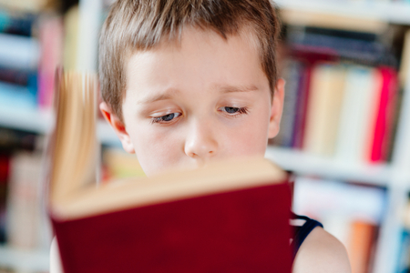 Seven years old boy reading a book in library. Child readingの写真素材