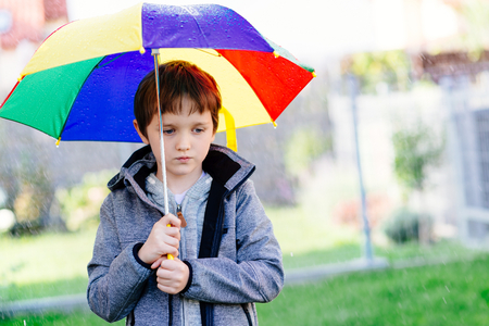 Seven years old boy standing at the rain with colorful umbrella.の写真素材
