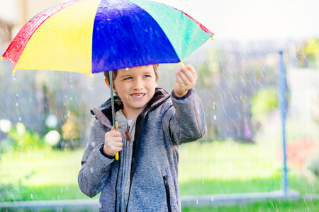 Seven years old boy standing at the rain with colorful umbrella.の写真素材