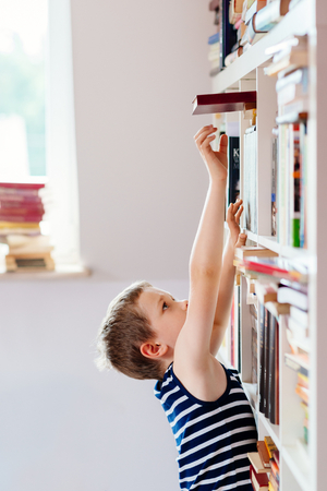 Seven years old boy reaching for book in library. Child readingの写真素材