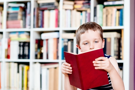 Seven years old boy reading a book in library. Child readingの写真素材