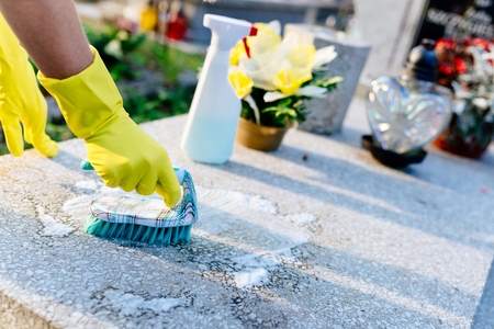 A woman cleans the grave. Washing tombstone with brush. Preparations for All Saints Day on November 1の写真素材