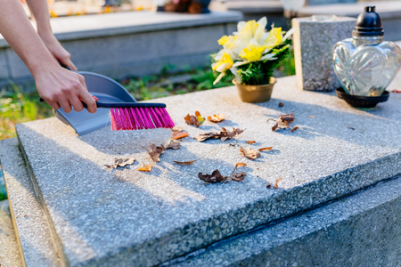 A woman cleans the grave. Sweeps leaves from the tombstone. Preparations for All Saints Day on November 1の写真素材