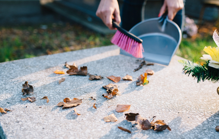 A woman cleans the grave. Sweeps leaves from the tombstone. Preparations for All Saints Day on November 1の写真素材