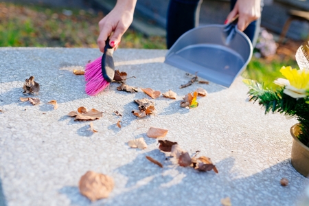 A woman cleans the grave. Sweeps leaves from the tombstone. Preparations for All Saints Day on November 1の写真素材