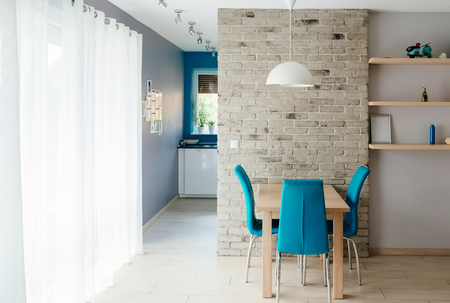 Modern dining room with wooden table, turquoise leather chairs, old empty grey brick wall and shelvesの写真素材