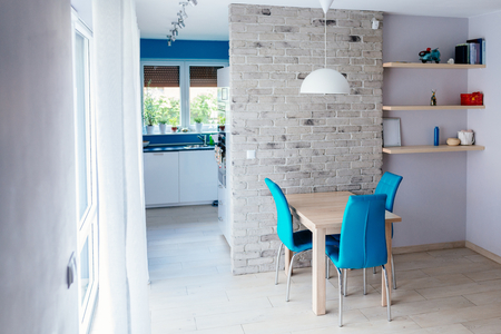 Modern dining room with wooden table, turquoise leather chairs, old empty grey brick wall and shelvesの写真素材