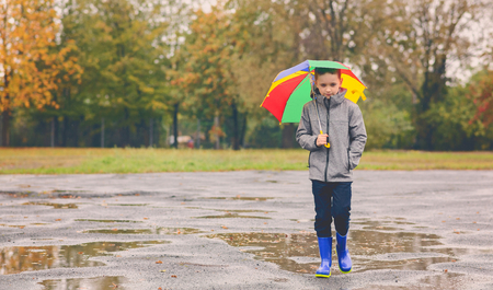 Sad child walking in rubber wellingtons on wet footpath. Rainy autumn day.の写真素材