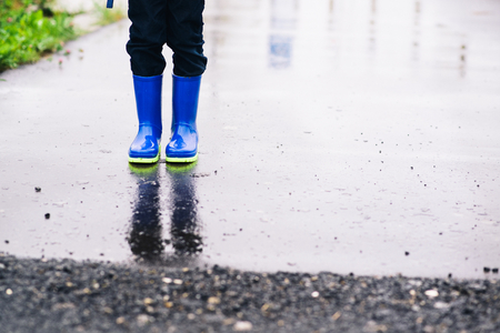 Child standing in rubber wellingtons on wet footpath. Rainy autumn day.の写真素材