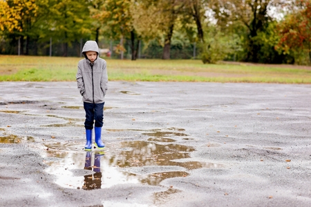 Sad little boy in rubber blue rain boots walking in the rain. Rainy autumn dayの写真素材