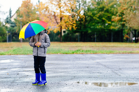 Sad child walking in rubber wellingtons on wet footpath. Rainy autumn day.の写真素材