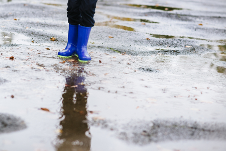 Happy little boy in rubber blue rainboots jumping to dirty puddle. Rainy autumn dayの写真素材