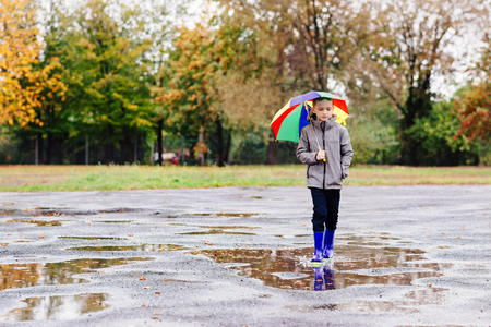 Sad child walking in rubber wellingtons on wet footpath. Rainy autumn day.の写真素材