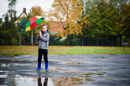 Sad child walking in rubber wellingtons on wet footpath. Rainy autumn day.の写真素材