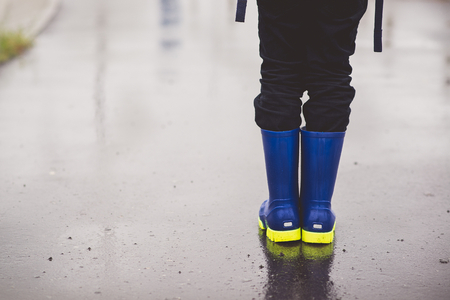 Child standing in rubber wellingtons on wet footpath. Rainy autumn day.の写真素材